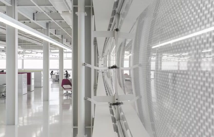 A sleek, modern interior with white structural elements and a curved security scanner or similar device, possibly within the Devine Detailing Chicago facility, featuring a spacious and minimalist design with a few purple chairs and employees in the background.