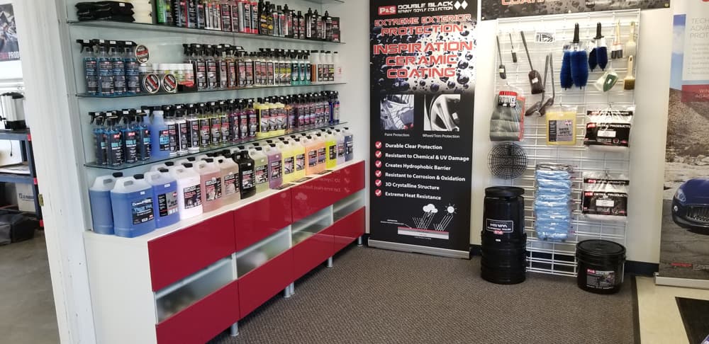 A display of auto detailing products, including various bottles of cleaning solutions and detailing supplies, is organized on shelves and racks outside an auto detailing business storefront.